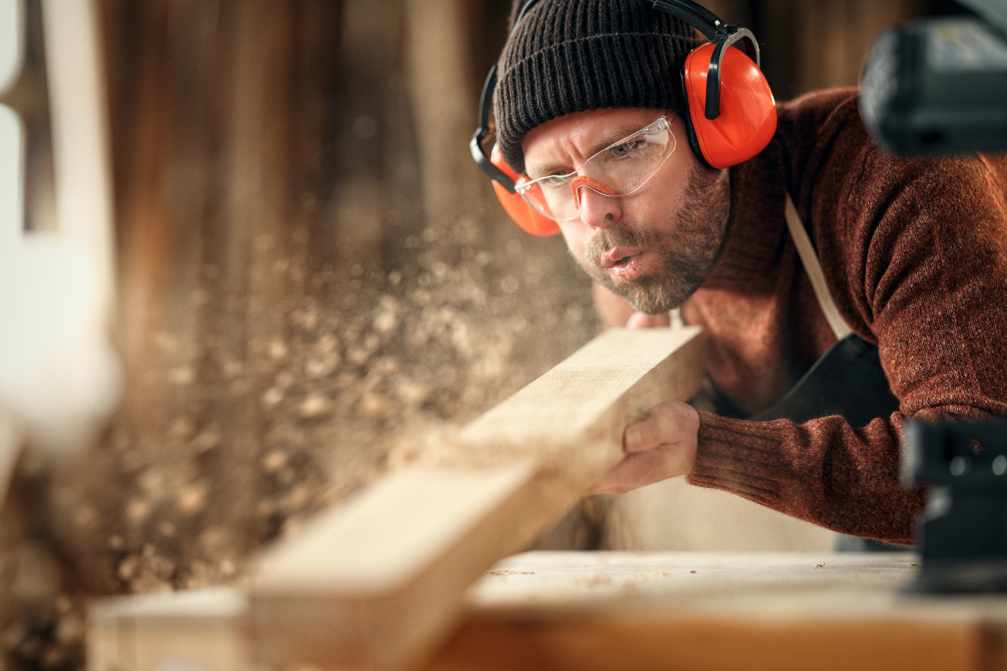 Handwerker mit Gehörschutz und Schutzbrille bei der Holzbearbeitung
