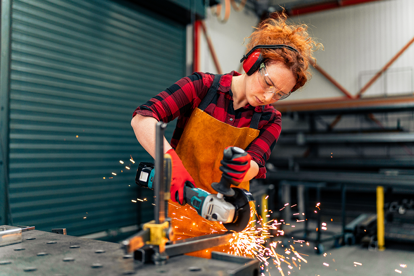 Frau mit Schutzausrüstung beim Metallschleifen in der Werkstatt