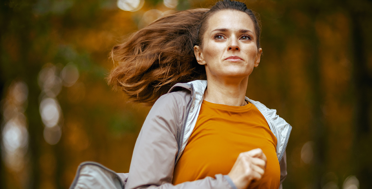 Frau joggt entschlossen durch einen herbstlichen Wald