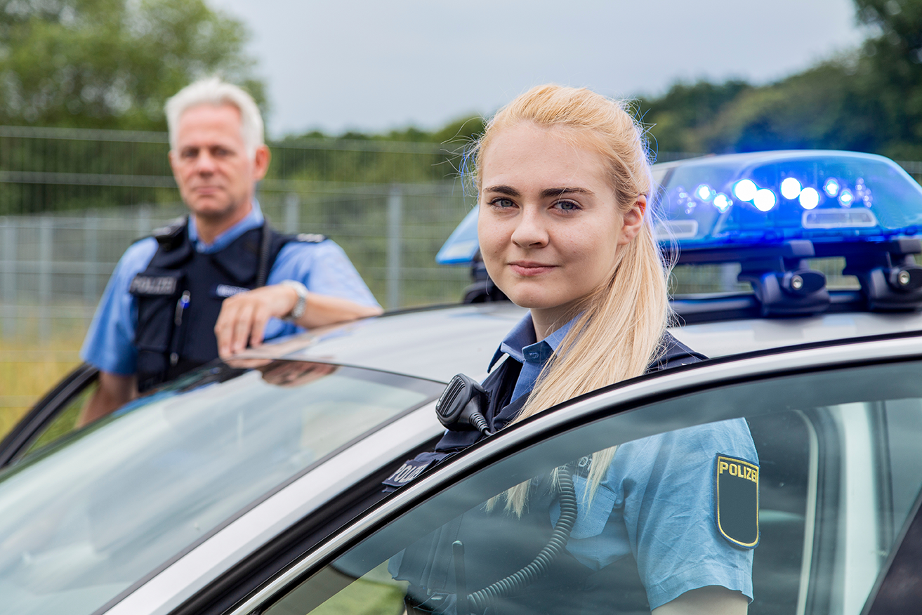 Zwei Polizeibeamte neben einem Streifenwagen mit Blaulicht