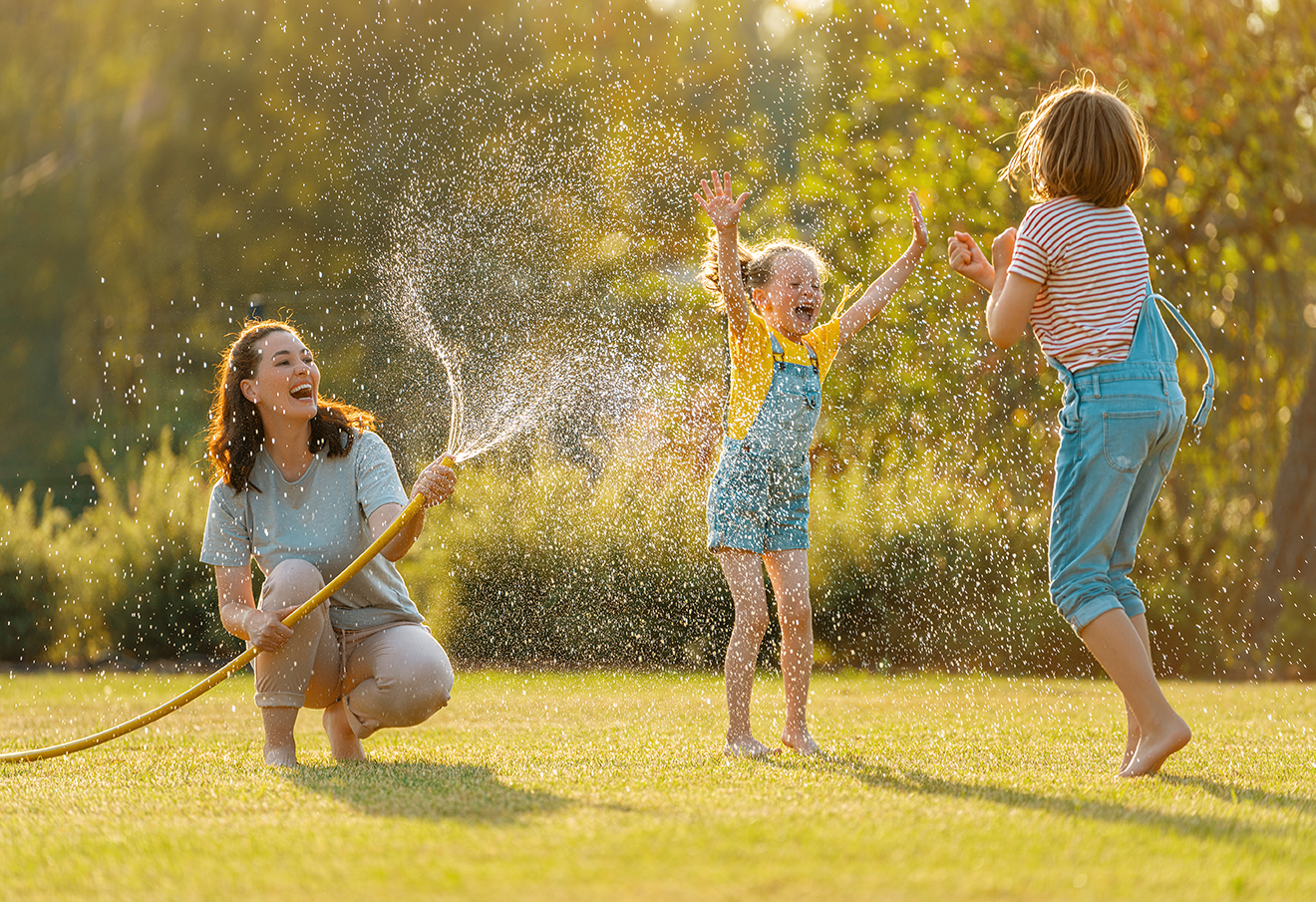 Mutter und Kinder spielen mit Gartenschlauch im Sonnenschein