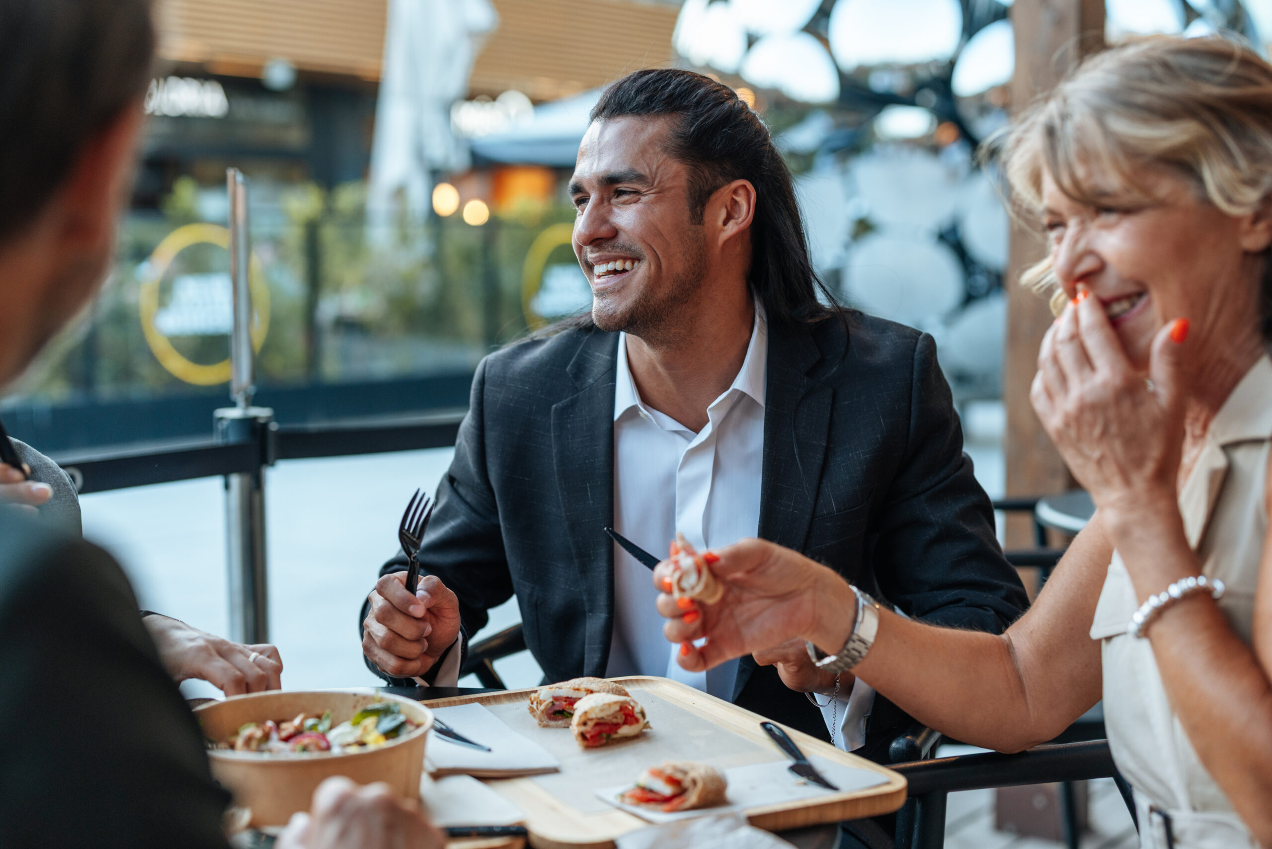 Zwei Personen in Business-Kleidung lachen gemeinsam beim Mittagessen im Freien.