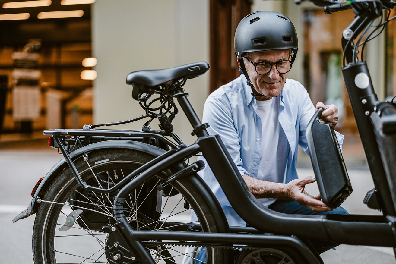 Älterer Mann mit Helm kontrolliert den Akku seines E-Bikes