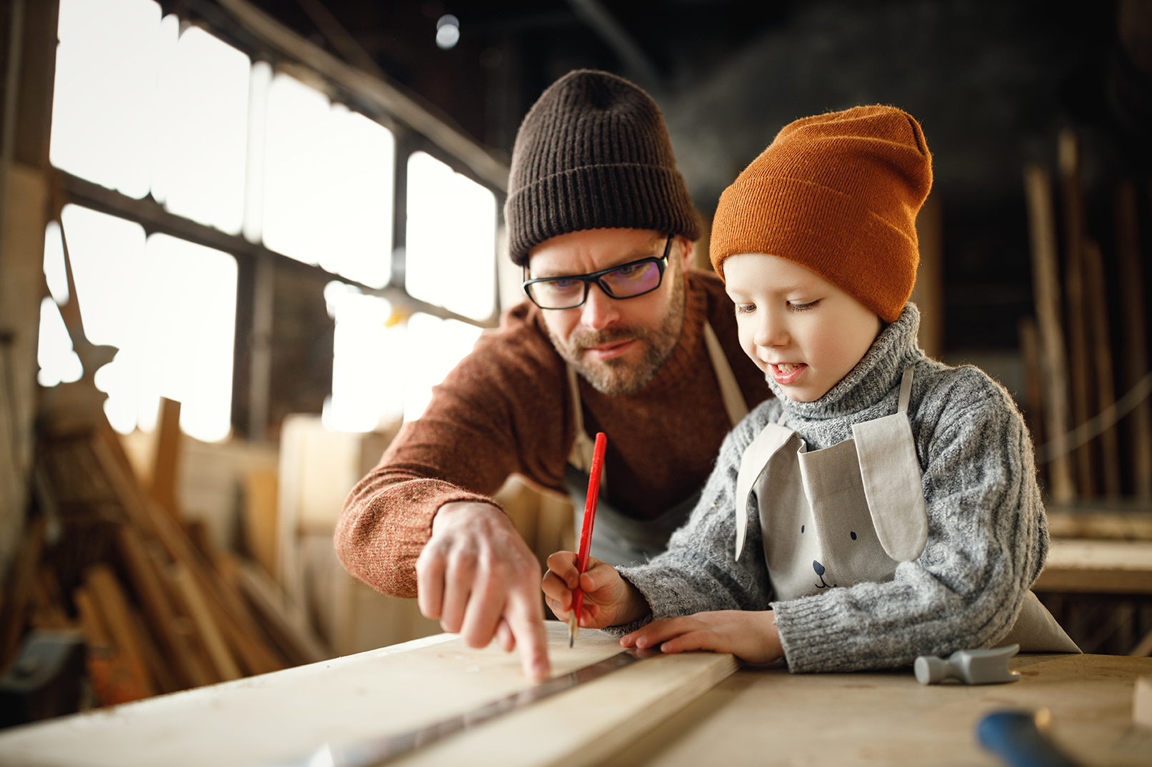 Vater zeigt Kind in der Werkstatt, wie man Holz anzeichnet
