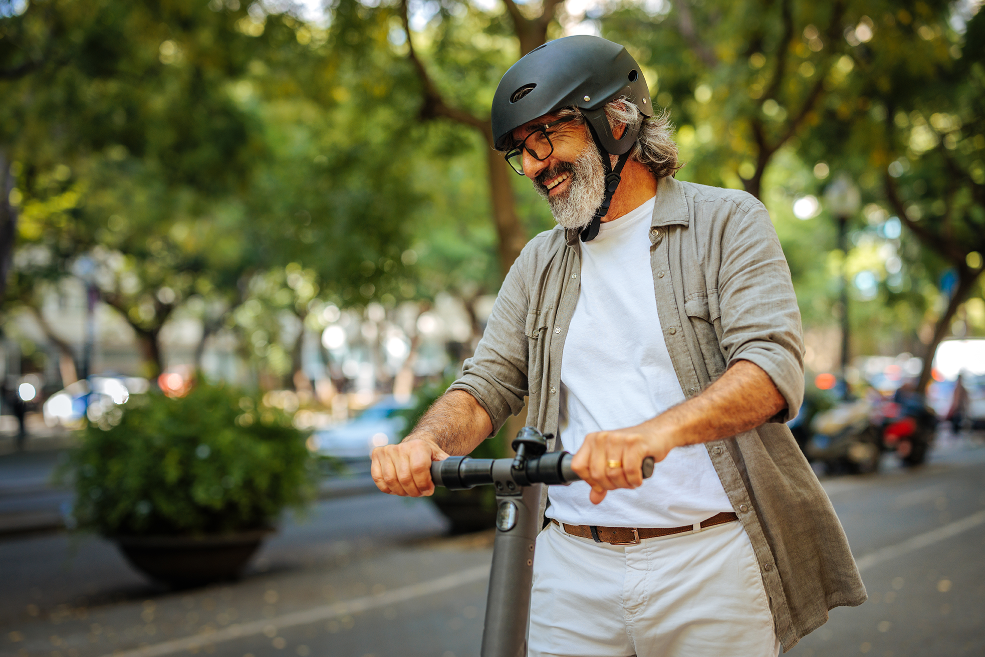 Älterer Mann fährt lächelnd mit Helm auf einem E-Scooter in der Stadt