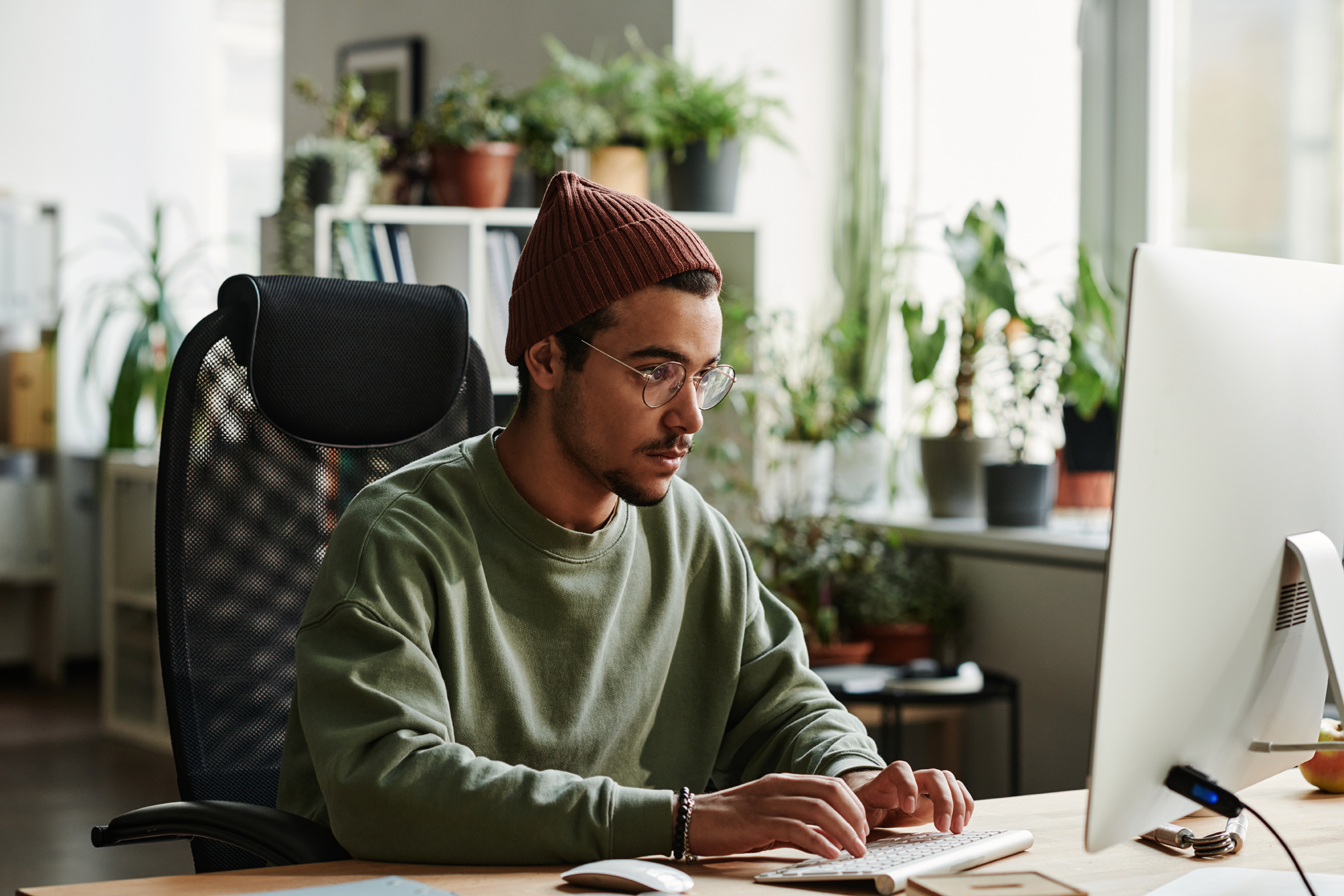 Junger Mann arbeitet konzentriert am Desktop-Computer im Homeoffice