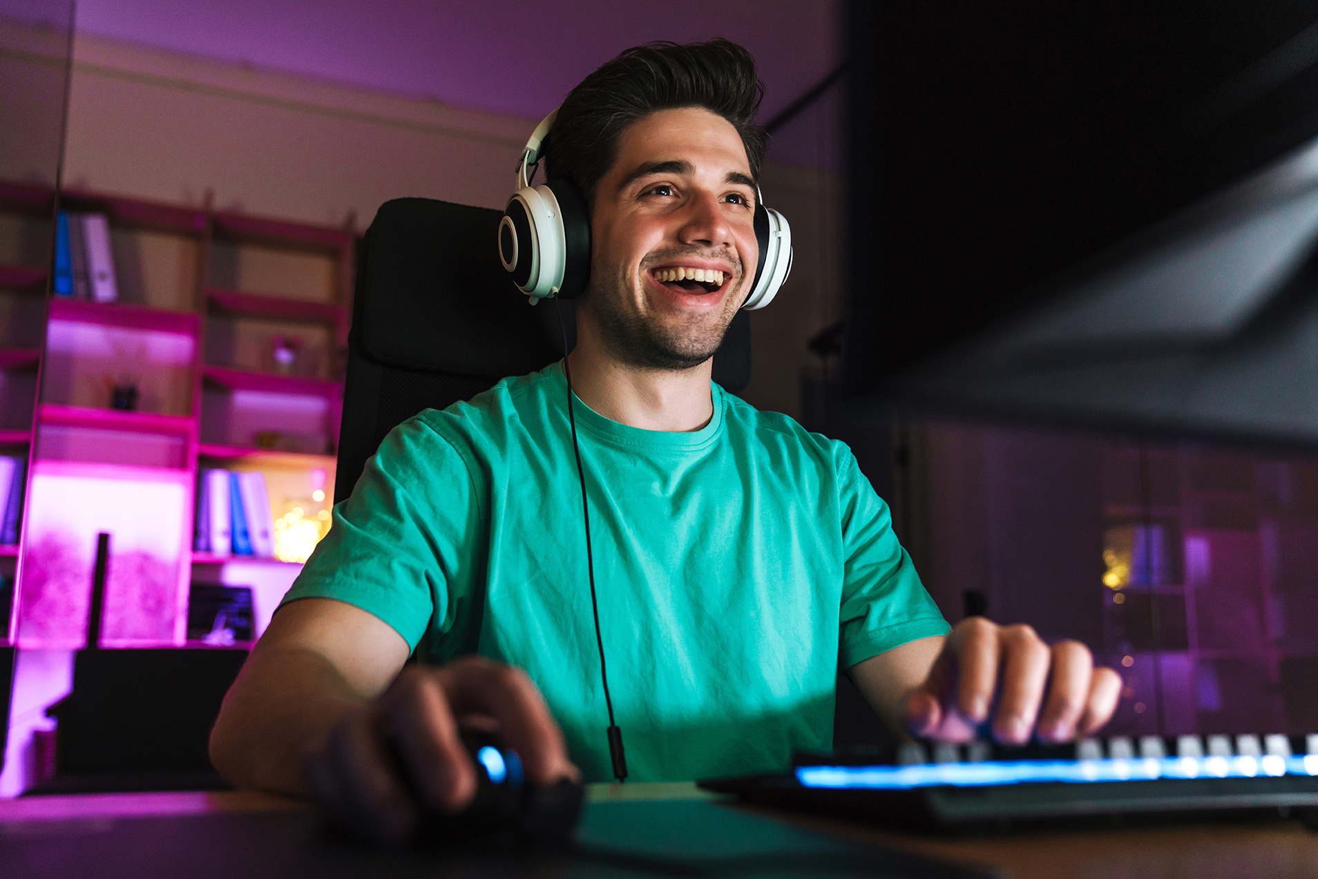 Junger Mann spielt begeistert mit Headset an seinem Gaming-PC