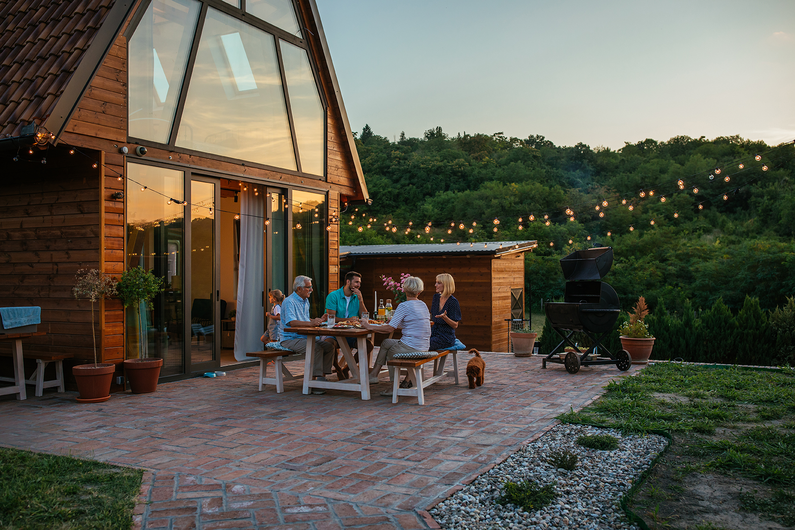 Familie sitzt gemeinsam auf der Terrasse eines modernen Holzhauses im Abendlicht